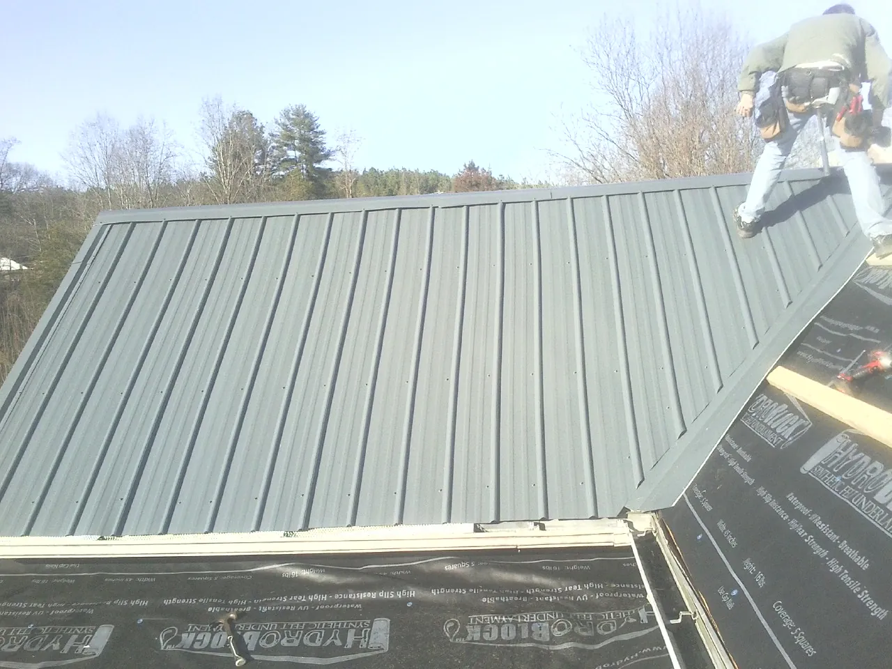 Crew installing dark green standing seam panels over synthetic underlayment in Elburn