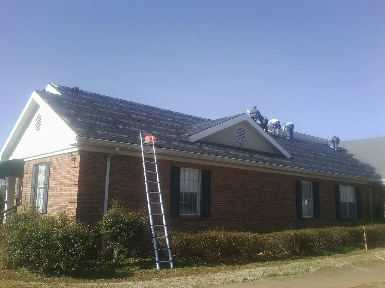 Crew tearing shingles off a brick ranch roof with a ladder set — Metal Roof Repair work by our crew in Elburn