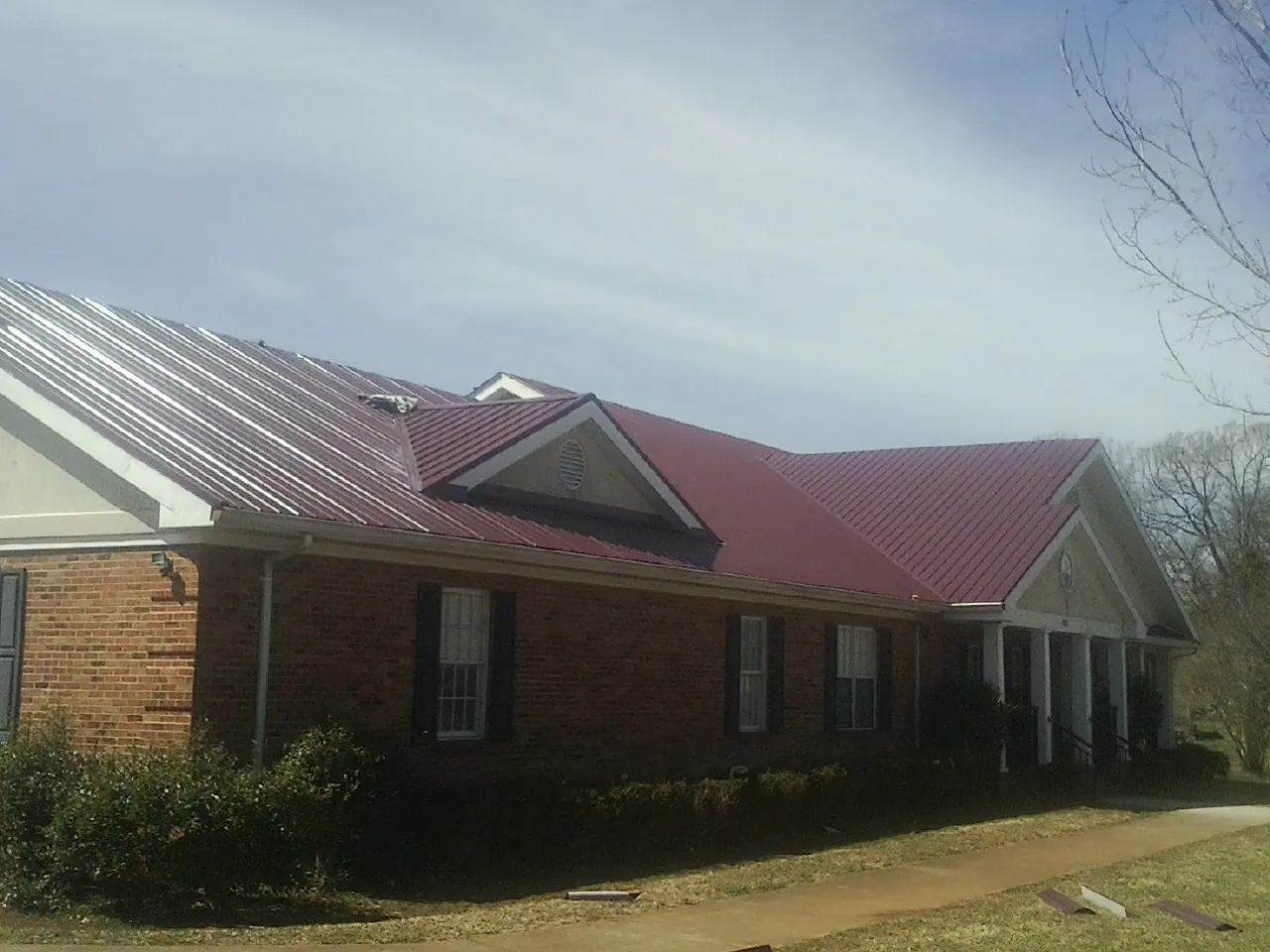 Red metal roof with gabled entries on a long brick building, from a Hail Damage Roof Repair job in Elburn