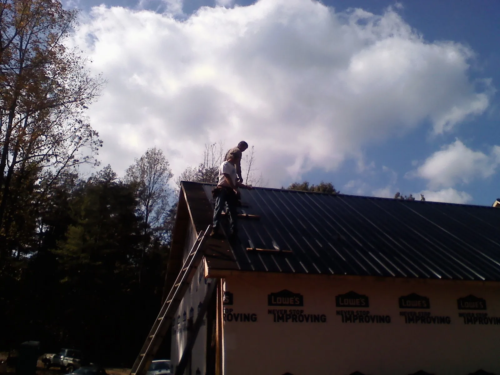 Roofer fastening dark metal panels high against a cloudy sky, from a Roof Inspection job in Elburn