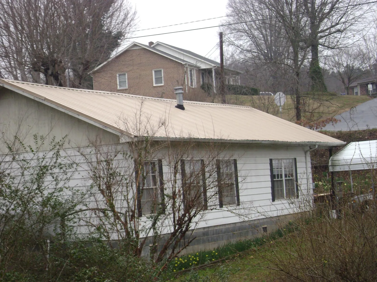 Tan metal roof on a white sided house set into a hillside — Commercial Roofing by Roofing Brothers in Elburn